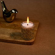 Decorative gold candle holder with lit candle on wooden tray, metallic bird figurine in background